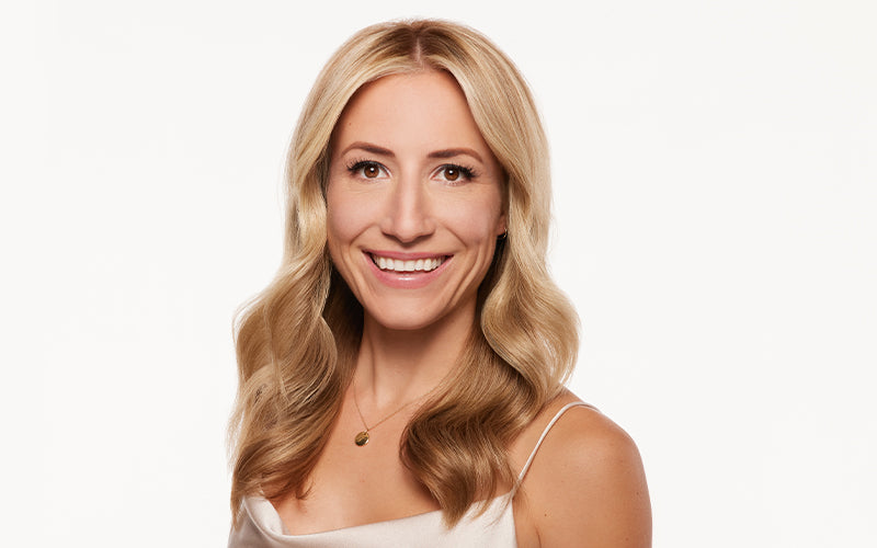 A smiling woman with voluminous, long blonde wavy hair shown from the shoulders up against a white background. Featured image for blog post: Step by Step: Voluminous Smooth Hair Blow Dry on Fine Hair
