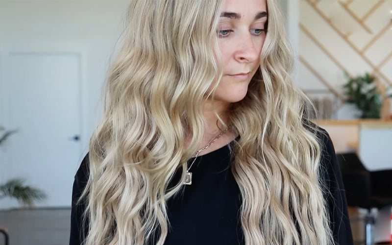 Side profile of a woman with long, voluminous platinum blonde wavy hair cascading past her shoulders against a dark background. Featured image for blog post: Back to Blonde: Hit Refresh on Your Hair