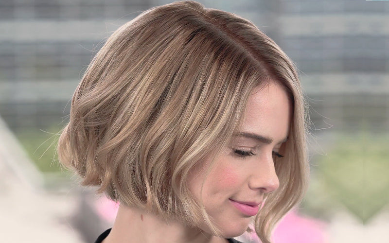 A woman with a short, chin-length blonde bob viewed from the side, hair neatly parted and smoothly styled with a clean, polished finish. Featured image for blog post: How To Part Your Hair According to Your Face Shape