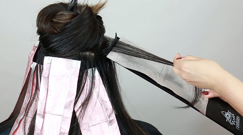 A close-up action shot of a gloved hand pulling a foil through the teeth of a highlighting comb during a color service on dark hair. Featured image for blog post: Meet The Kenra Education Team’s 5 Must-Have Hairstyling & Coloring Tools 