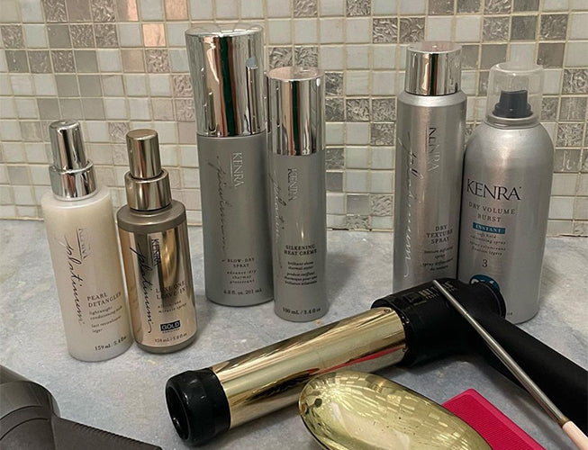 A flat lay of several tall silver and gold Kenra Professional haircare bottles and styling product tubes arranged together on a surface. Featured image for blog post: Recreate Lily James' Met Gala 2022 Hairstyle in 6 Simple Steps with Kenra Professional P