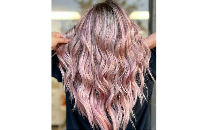 Back view of long, flowing waves in a soft rose gold and pink color, with the hue shifting from a warm blush at the roots to a brighter pink through the mid-lengths and ends. Featured image for blog post: Pink Hair, We Care 