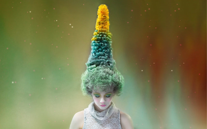 A model wearing a dramatic sculptural headpiece in green and yellow tones resembling tall, textured foliage or an abstract tree form, styled with pale editorial makeup. Featured image for blog post: Sickening Styles and the People Behind Them: A Multi-Par