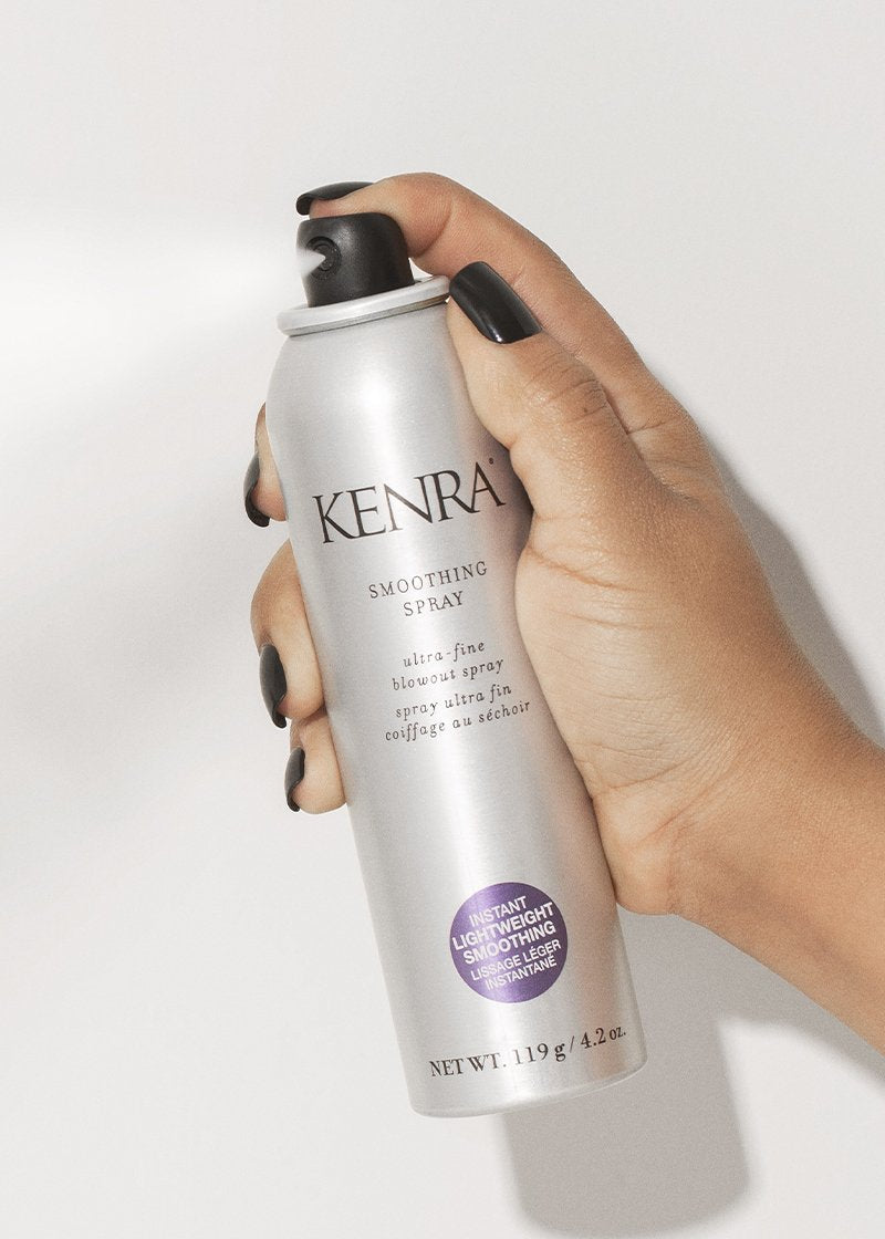 A hand holds up a white aerosol can of Kenra-branded smoothing spray against a plain light background, with the label and nozzle clearly visible. Featured image for blog post: Switch Your Haircare Routine to Adjust to the Elements 